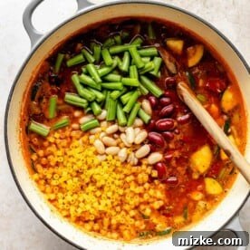 Stirring beans, green beans, and pasta into minestrone soup.