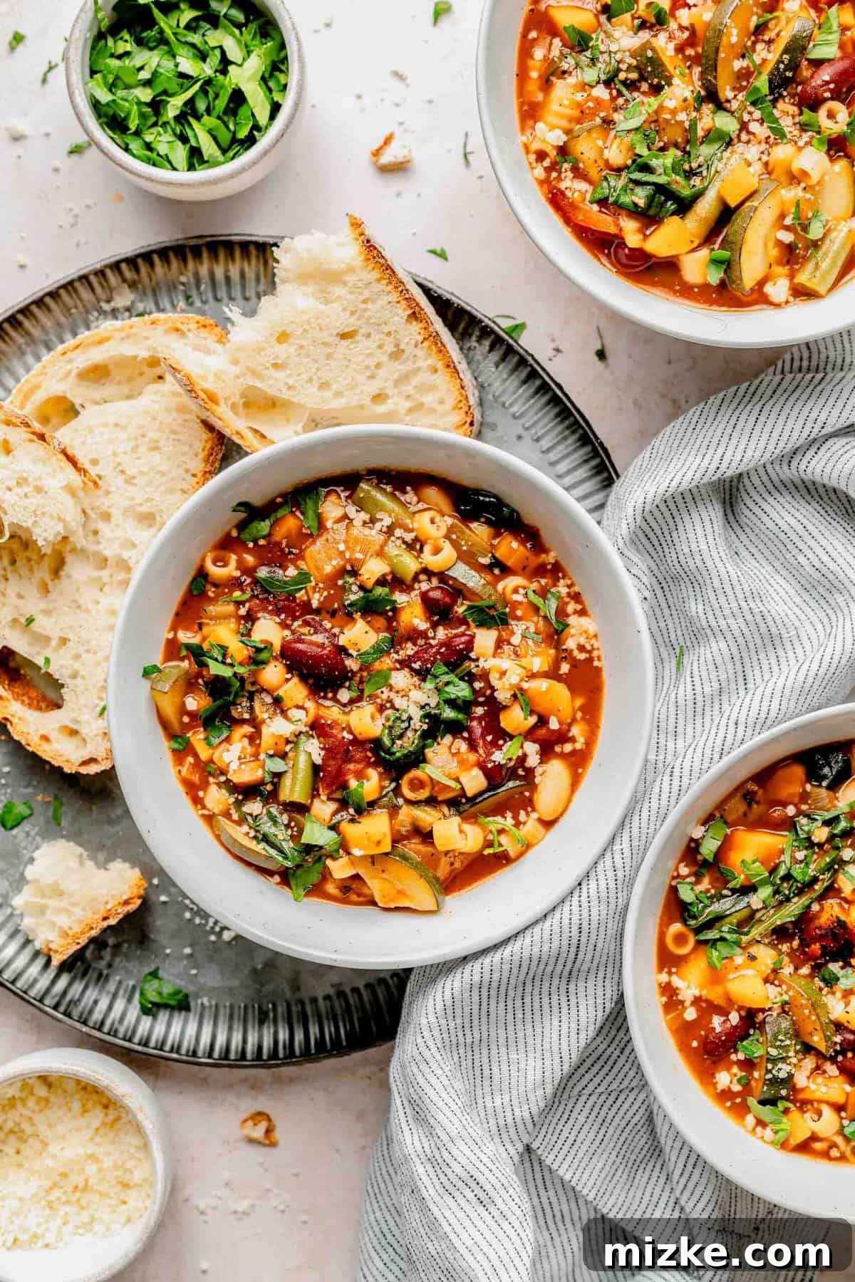 Loaded with tender veggies, beans, and pasta in a flavorful, tomato-y broth, minestrone soup is the perfect vegetarian main. Overhead shot of three bowls of minestrone soup, garnished and served with slices of crusty bread.