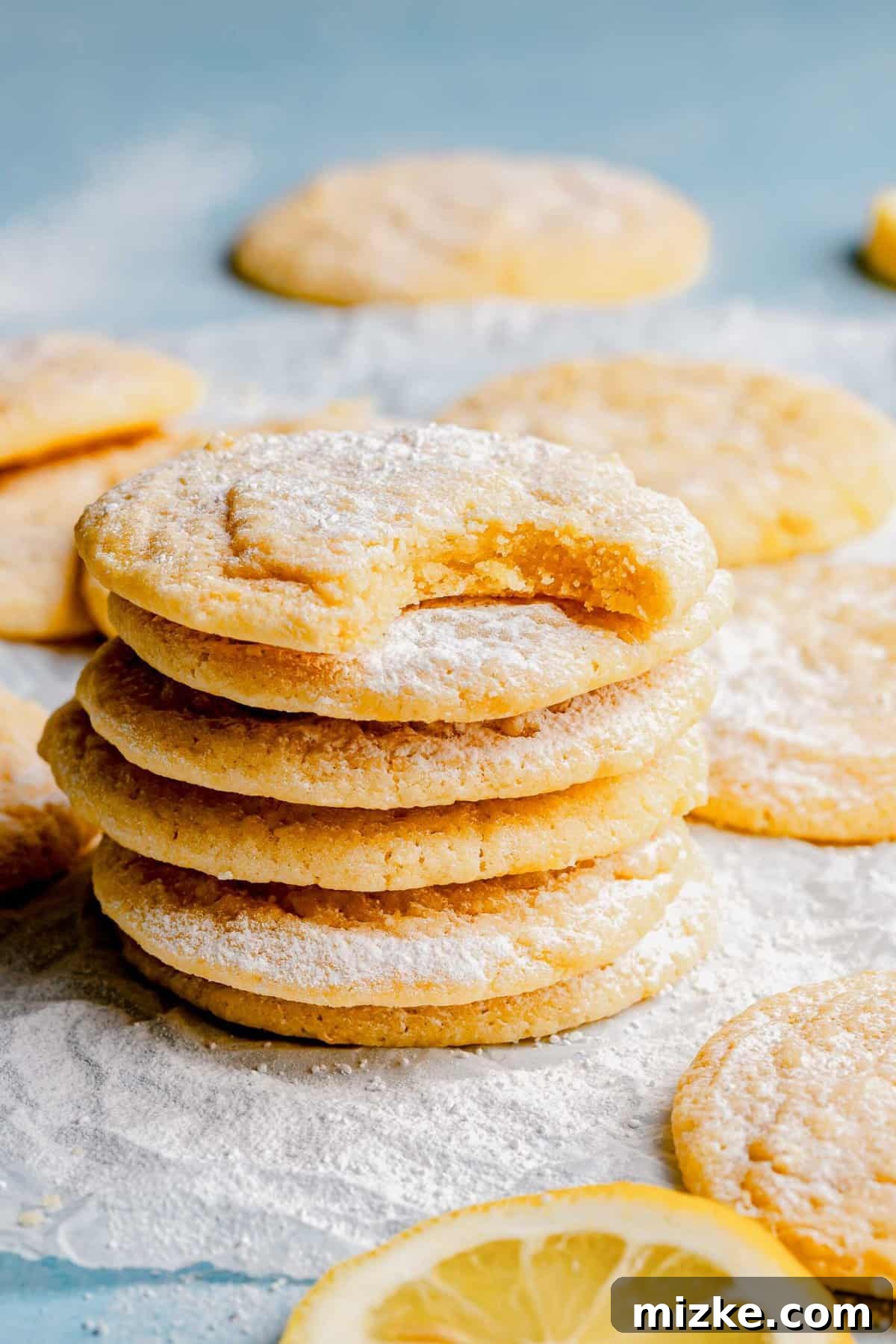 Golden lemon cookies with a perfect balance of crisp and chewiness. A stack of golden lemon cookies on a white surface. The top cookie has a bite taken out, revealing its soft interior and demonstrating the perfect chewy texture.