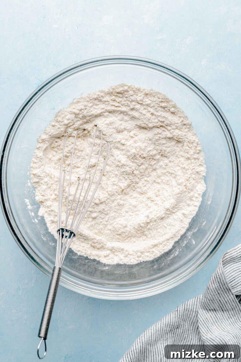 Whisk dry ingredients thoroughly for an evenly distributed cookie dough. A large silver bowl filled with dry ingredients (flour, cornstarch, baking soda, salt) being whisked together by hand, creating a uniform white powder mixture.