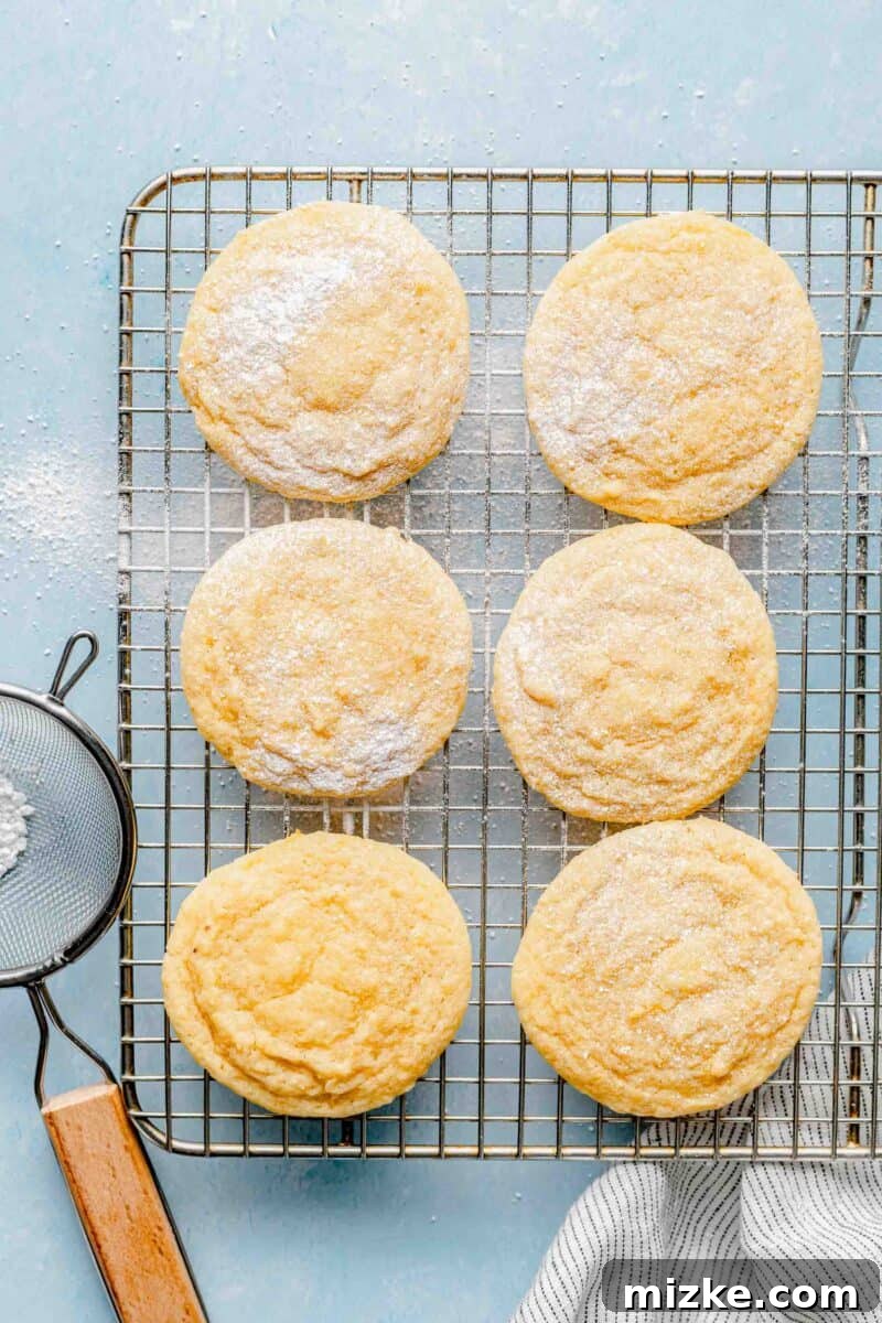 Allow cookies to cool completely before dusting with powdered sugar for a perfect finish. Freshly baked lemon cookies cooling on a wire rack, lightly dusted with powdered sugar, showcasing a crinkled top and ready to be enjoyed as a delightful treat.