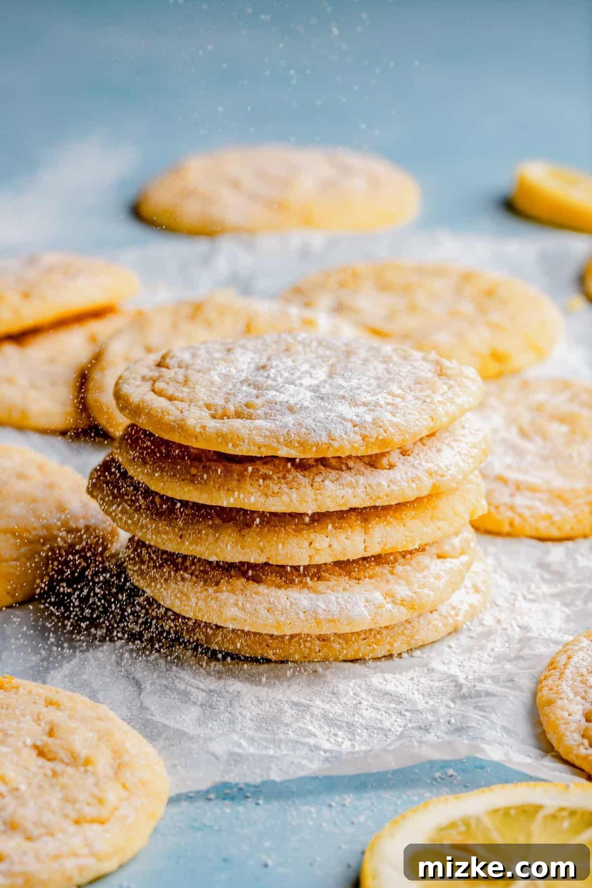 Enjoy these delightful lemon cookies with a perfect balance of crisp and chewiness. A beautifully arranged stack of six golden-yellow lemon cookies, perfectly round, with lightly crinkled tops and a dusting of powdered sugar, presented on a minimalist white background.