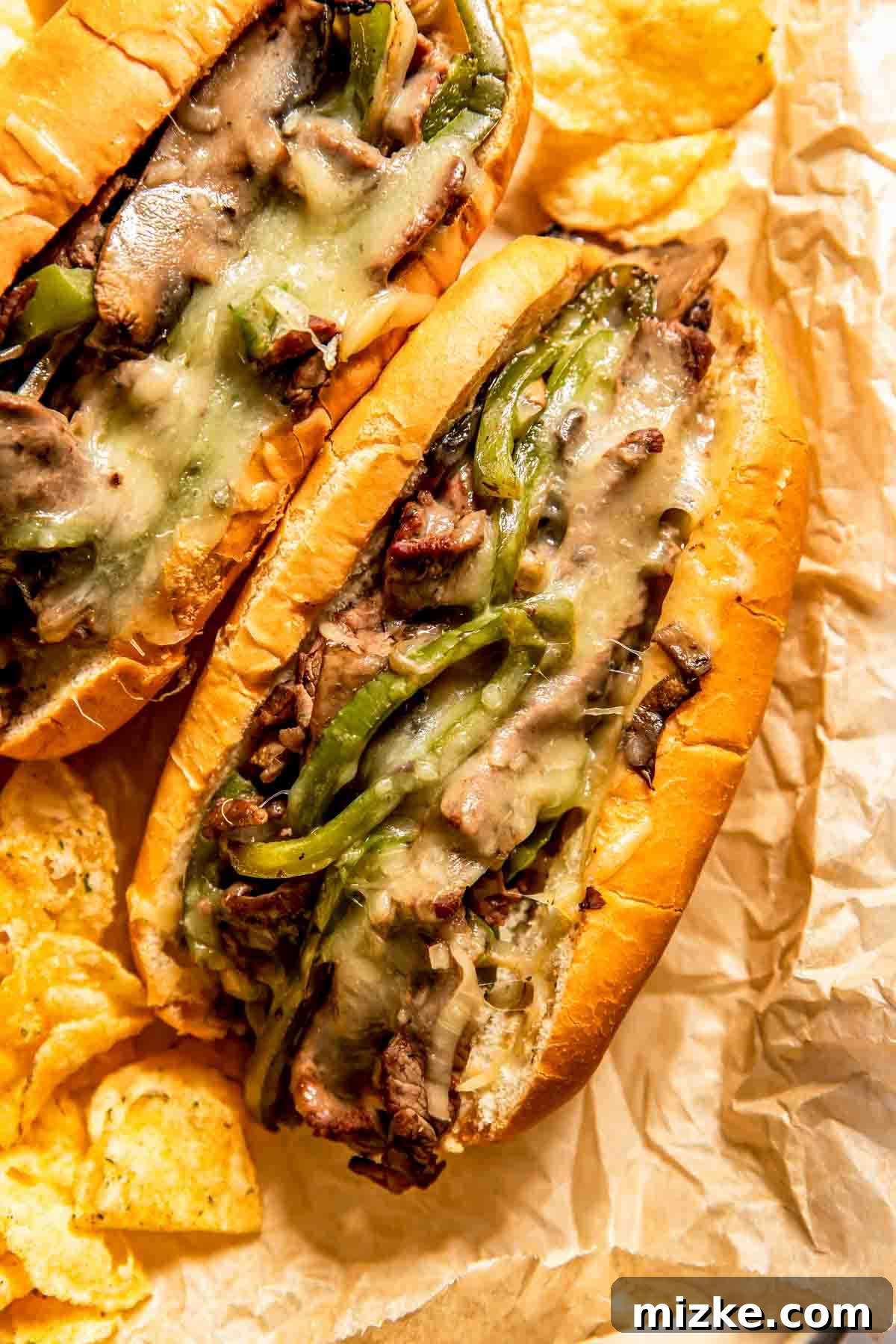 Philadelphia's Legendary Steak Sandwich 3 Two Philly cheesesteak sandwiches filled with sliced beef, melted cheese, mushrooms, and green peppers, served on parchment paper with potato chips.