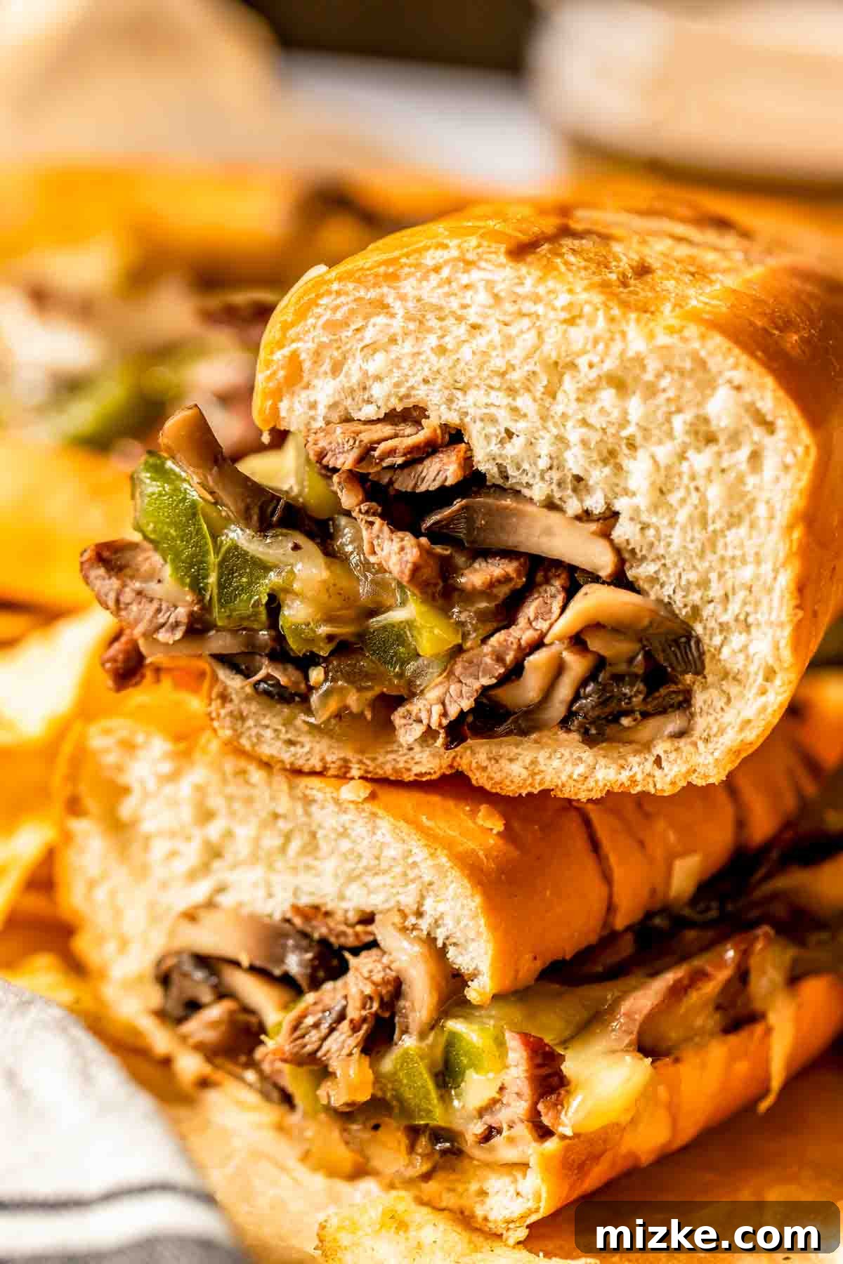 Philadelphia's Legendary Steak Sandwich 4 A close-up of a sandwich filled with sliced beef, melted cheese, mushrooms, and green bell peppers, cut in half and stacked.