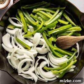Philadelphia's Legendary Steak Sandwich 6 Sliced green bell peppers and onions in a cast iron skillet with a wooden spoon, surrounded by small bowls of salt and pepper.