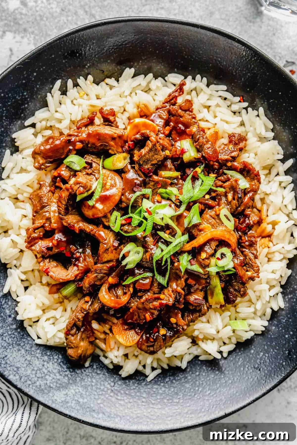 Thinly sliced beef, garlic, onions, and scallions are marinated in a flavorful sauce and fried to perfection in this Korean beef bulgogi. A serving of Korean beef bulgogi over steamed white rice in a rustic bowl.