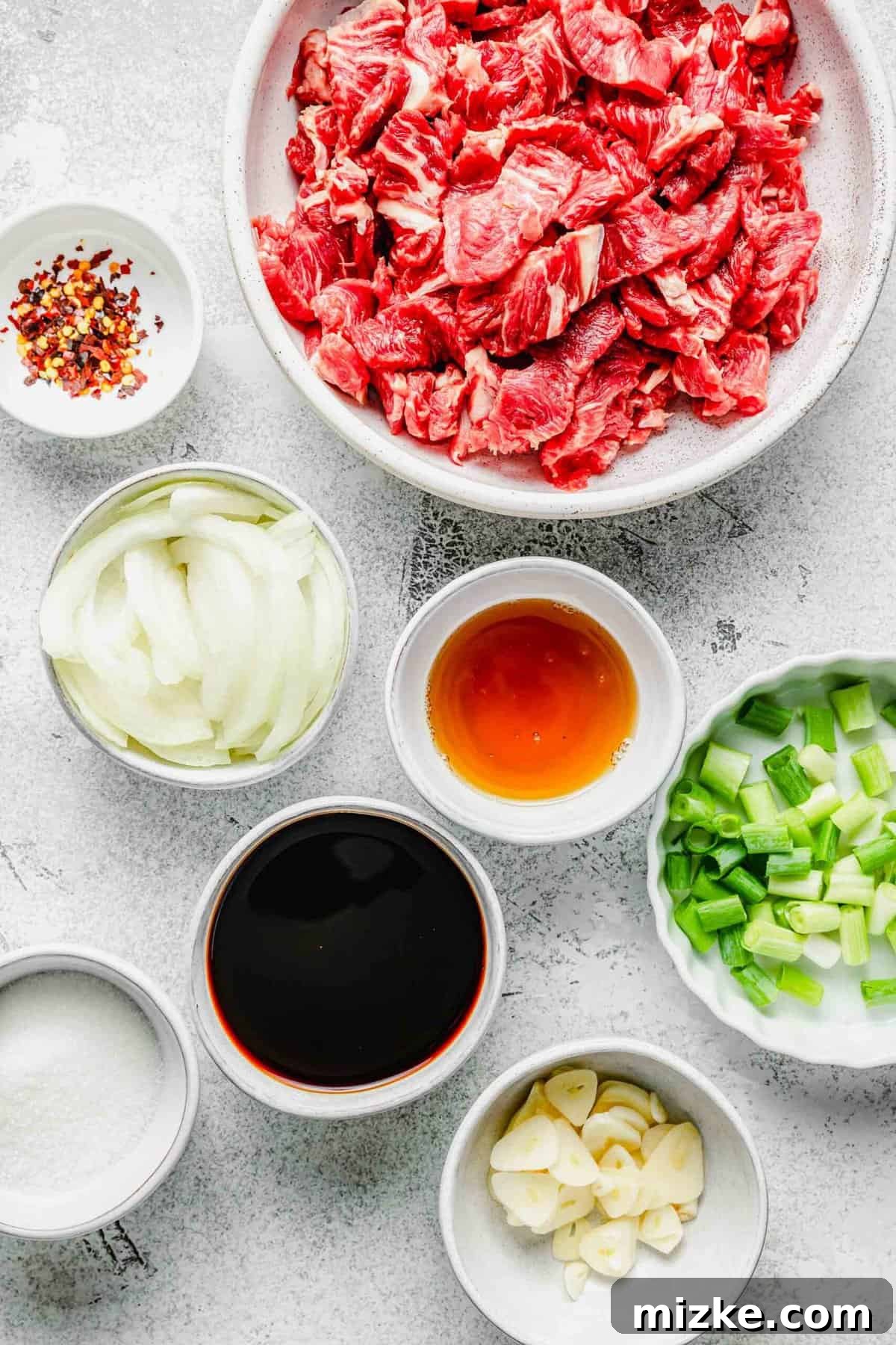 Thinly sliced beef, garlic, onions, and scallions are marinated in a flavorful sauce and fried to perfection in this Korean beef bulgogi. Individual ingredients for Korean beef bulgogi including thinly sliced beef, soy sauce, sesame oil, sugar, red pepper flakes, onion, garlic, and green onions, all arranged in small bowls.
