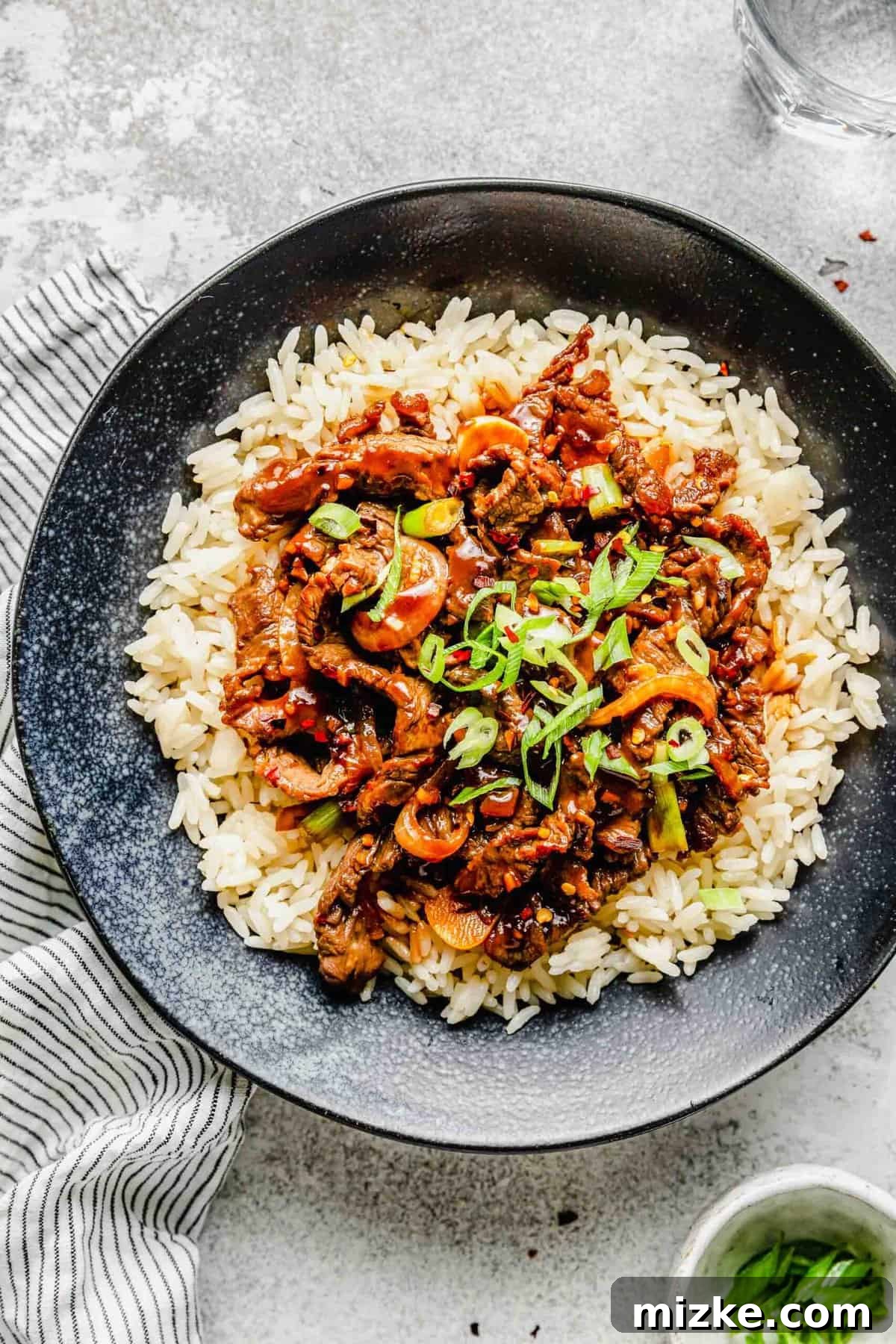 Thinly sliced beef, garlic, onions, and scallions are marinated in a flavorful sauce and fried to perfection in this Korean beef bulgogi. A bowl of Korean beef bulgogi over rice, garnished with green onions, next to a small bowl of sliced green onions and a pair of chopsticks.