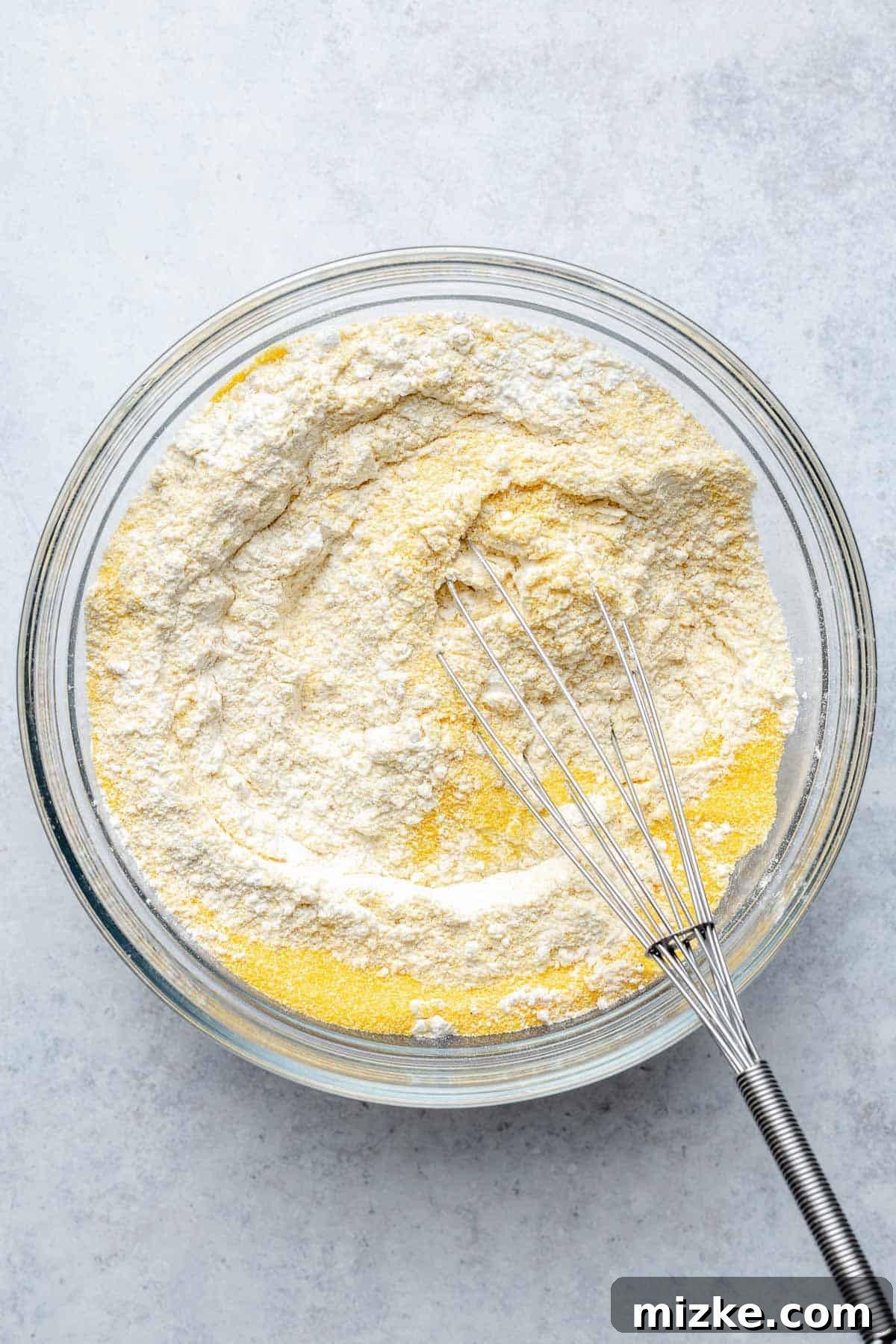 A bowl containing all-purpose flour, cornmeal, baking powder, and salt, freshly whisked together to combine dry ingredients for cornbread.