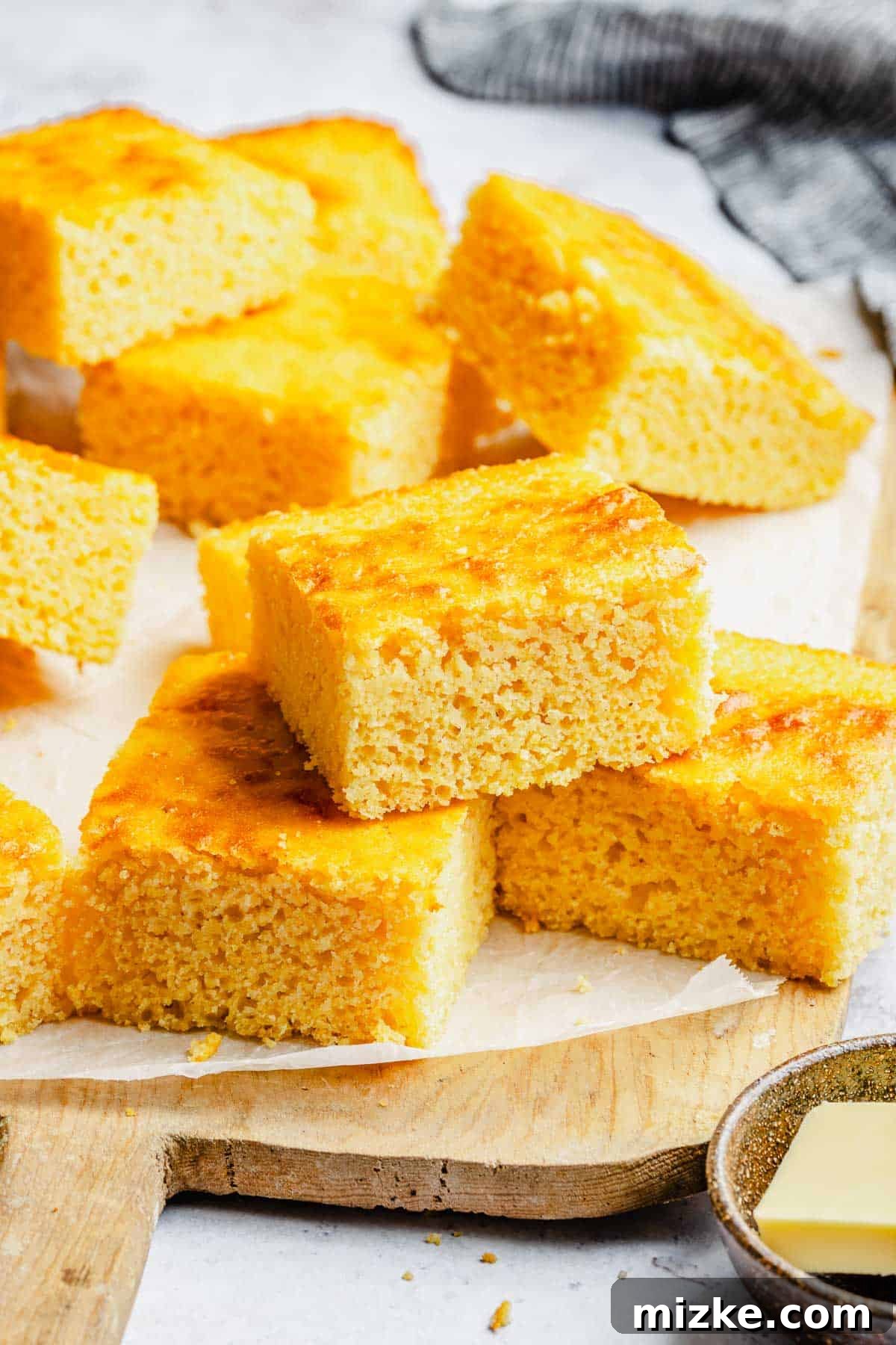 Beautifully stacked slices of homemade cornbread on a cutting board lined with parchment paper, showcasing their perfect texture and golden hue.