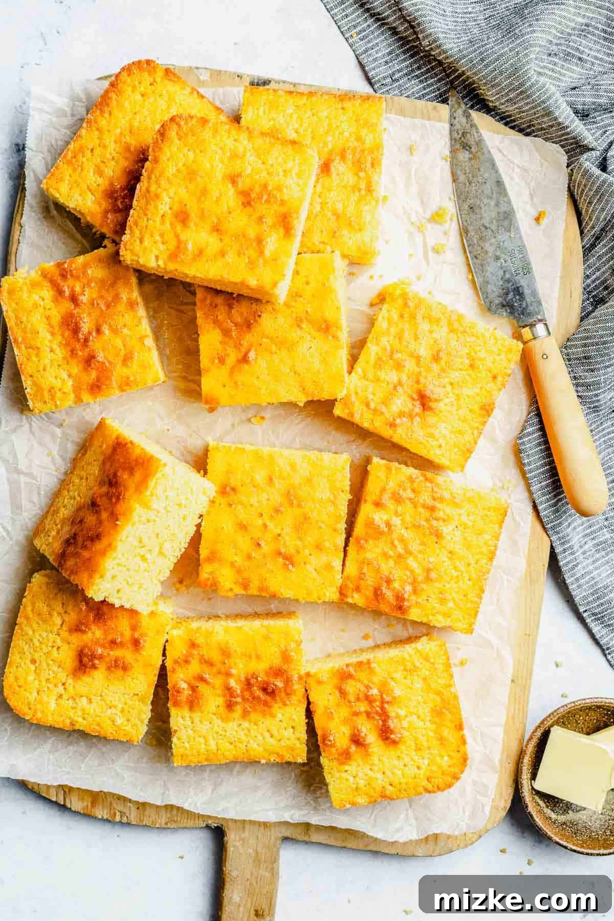 An inviting overhead shot of perfectly cut cornbread slices, carefully arranged on a cutting board lined with parchment paper, ready to be picked up and savored.
