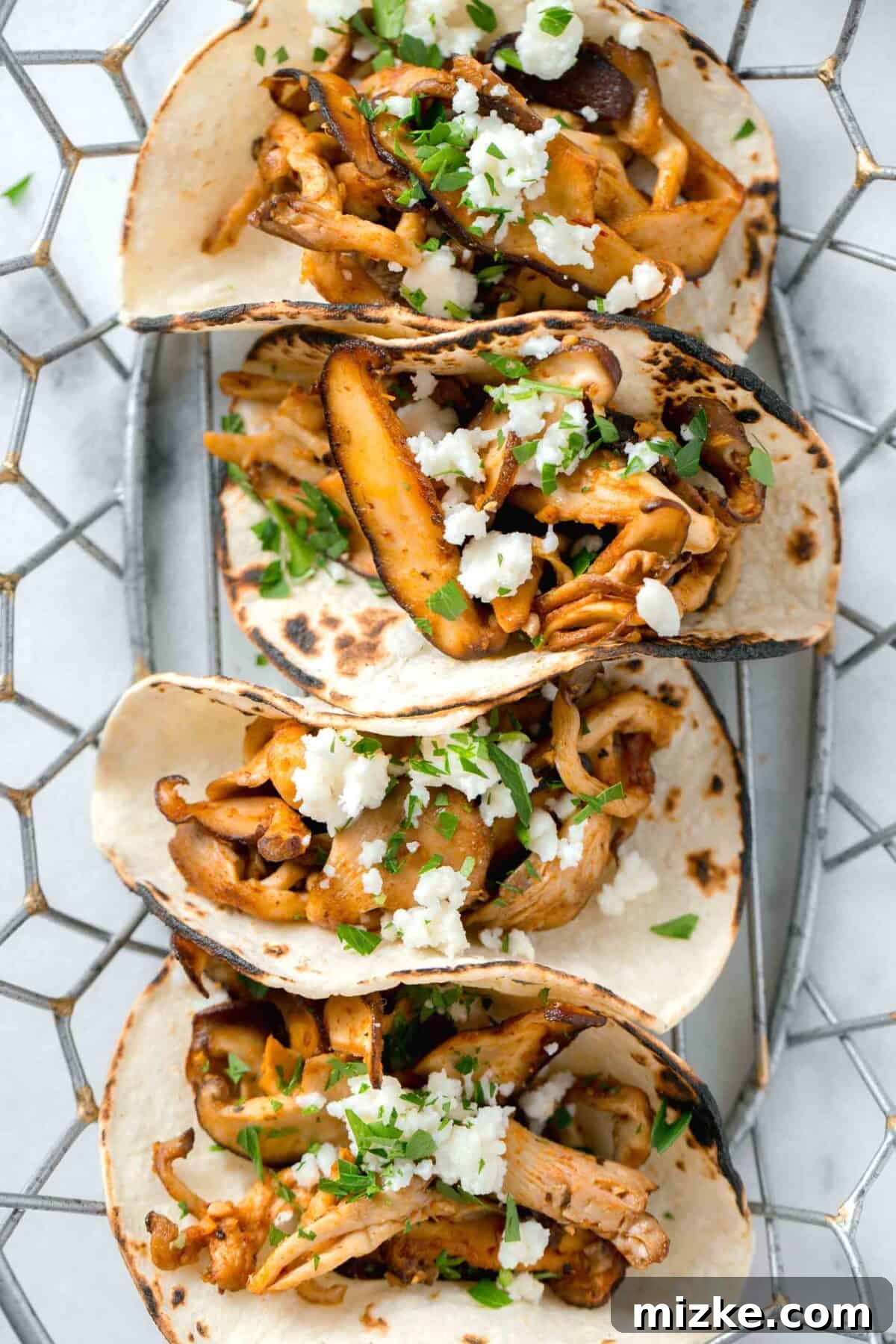 Umami Oyster Tacos 2 Stacked oyster mushroom tacos in a wire basket, garnished with fresh herbs and cotija cheese