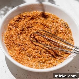 A metal whisk in burger seasoning on a small white dish, ready to be mixed or applied.