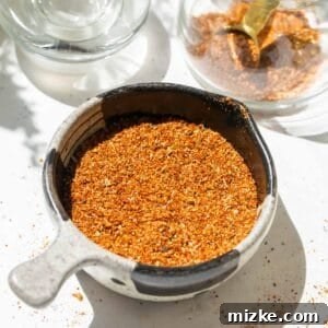 Homemade taco seasoning in a black and grey ceramic measuring cup, alongside a glass jar filled with the blend.