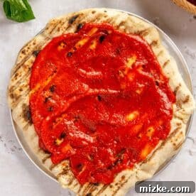 pizza sauce spread on top of grilled pizza dough