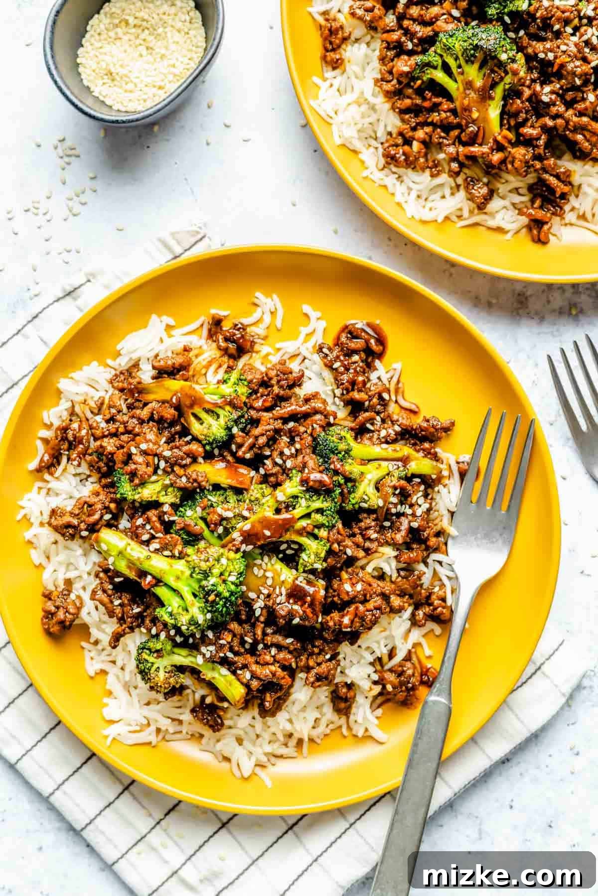 Savory Beef and Broccoli Skillet 2 Delicious ground beef and broccoli plated on bright yellow dishes, served over fluffy jasmine rice with a metal fork resting on the side.