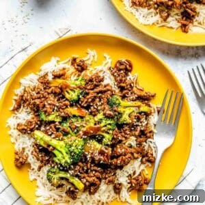 Ground beef and broccoli plated on bright yellow plates on a bed of jasmine rice with a metal fork on the plate