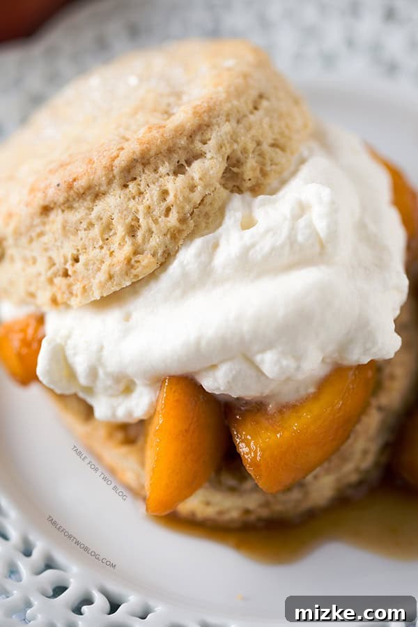 Layered Boozy Peaches and Honey Cream Shortcake Side angle shot of a single Boozy Peaches and Honey Cream Shortcake, showing layers of biscuit, peaches, and cream