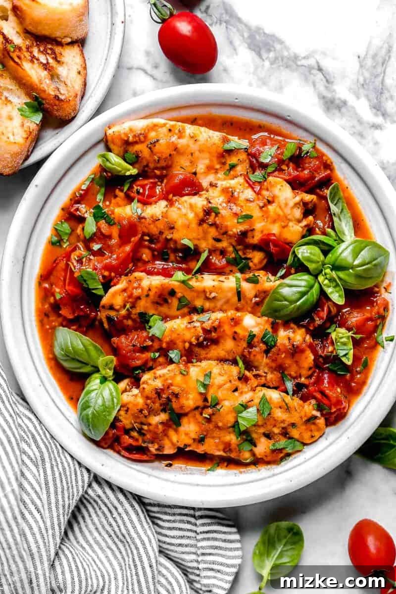 Sun-Kissed Tomato-Herb Chicken 2 Cooked chicken tenders resting on a bed of vibrant tomato herb sauce, garnished with fresh basil on a pristine white plate.