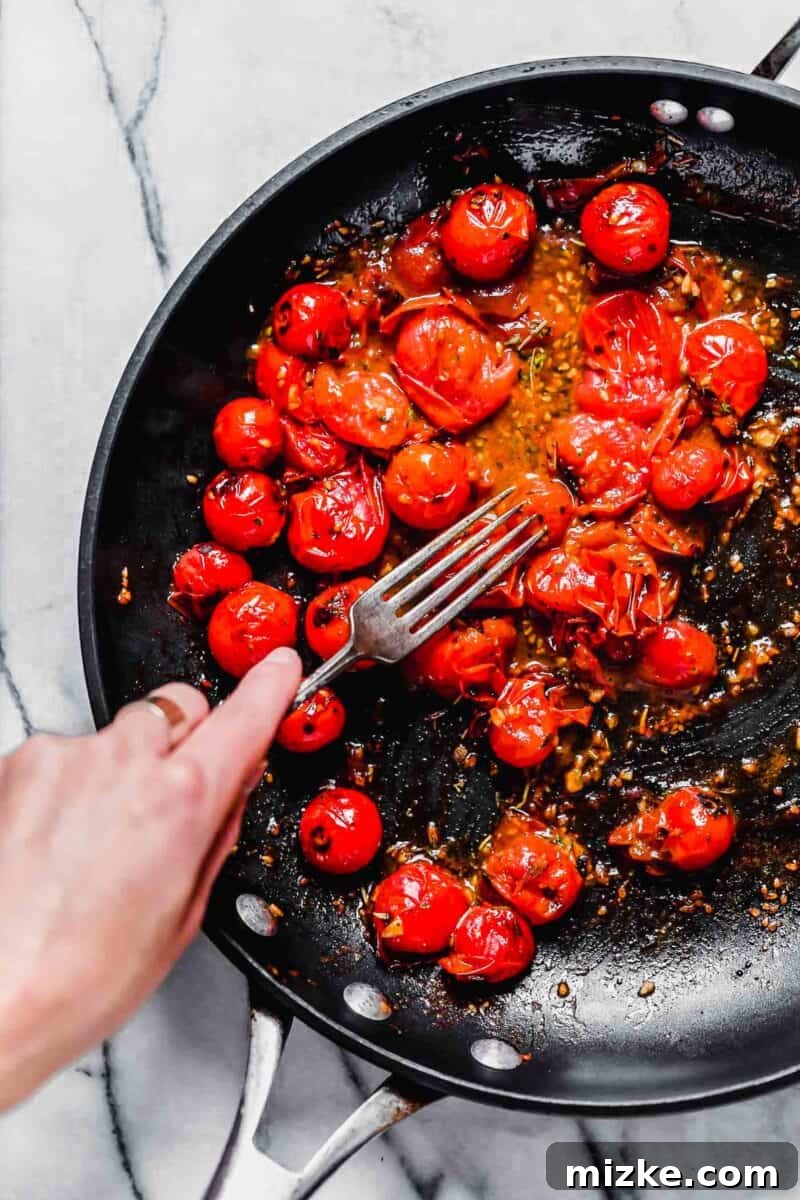 Sun-Kissed Tomato-Herb Chicken 7 A fork gently smashing cherry tomatoes in a nonstick skillet to release more juice and create a richer sauce.