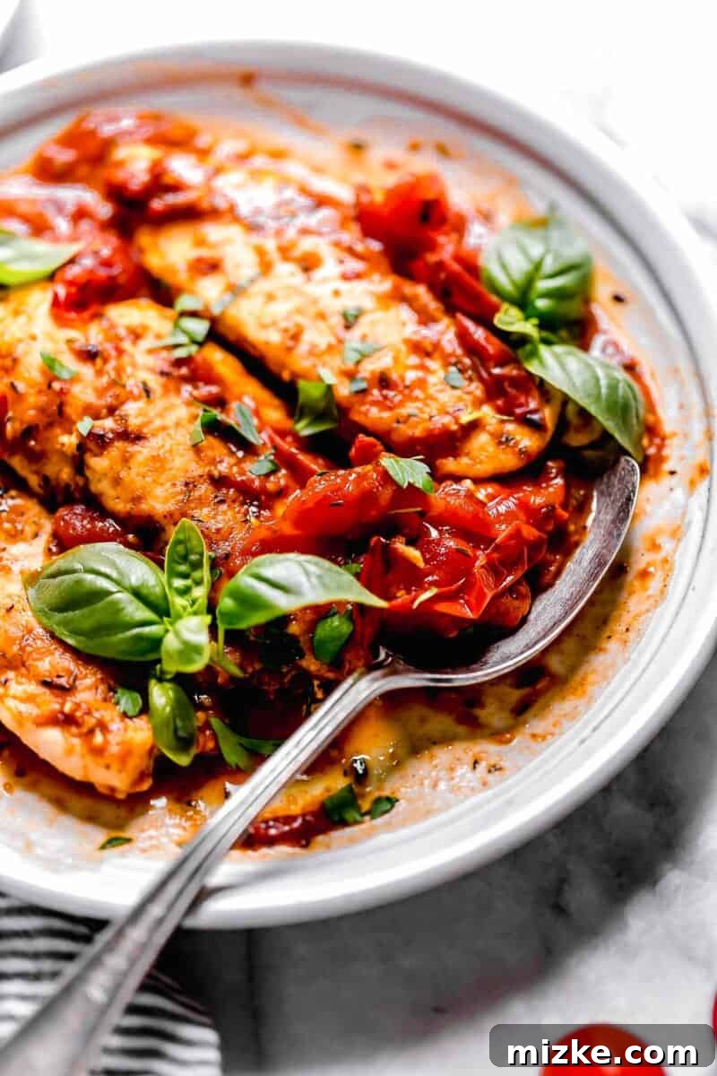 Sun-Kissed Tomato-Herb Chicken 8 A metal spoon scooping up vibrant tomato herb sauce next to perfectly cooked chicken tenders on a clean white plate.
