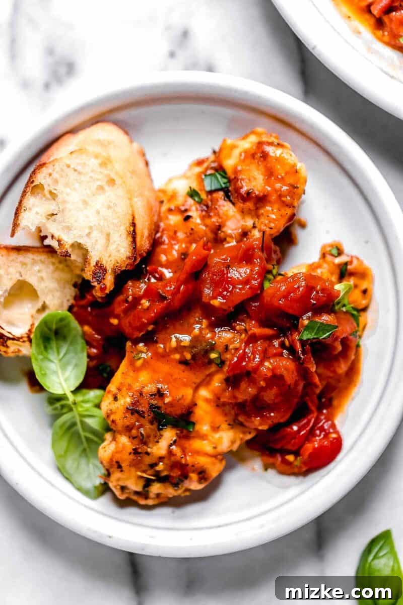 Sun-Kissed Tomato-Herb Chicken 9 Tomato herb pan sauce spread artistically over cooked chicken tenders on a small white plate, accompanied by toasted bread and fresh basil leaves.