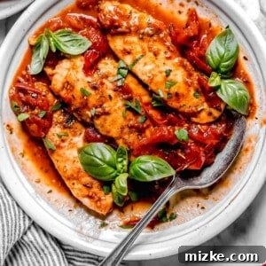 Sun-Kissed Tomato-Herb Chicken 10 Cooked chicken tenders on a bed of tomato herb sauce with fresh basil and a metal spoon on the side