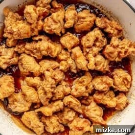 fried chicken added to the general tso's sauce in a cast iron skillet