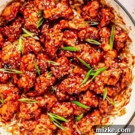 general tso's chicken in a cast iron skillet topped with white sesame seeds and fresh scallions