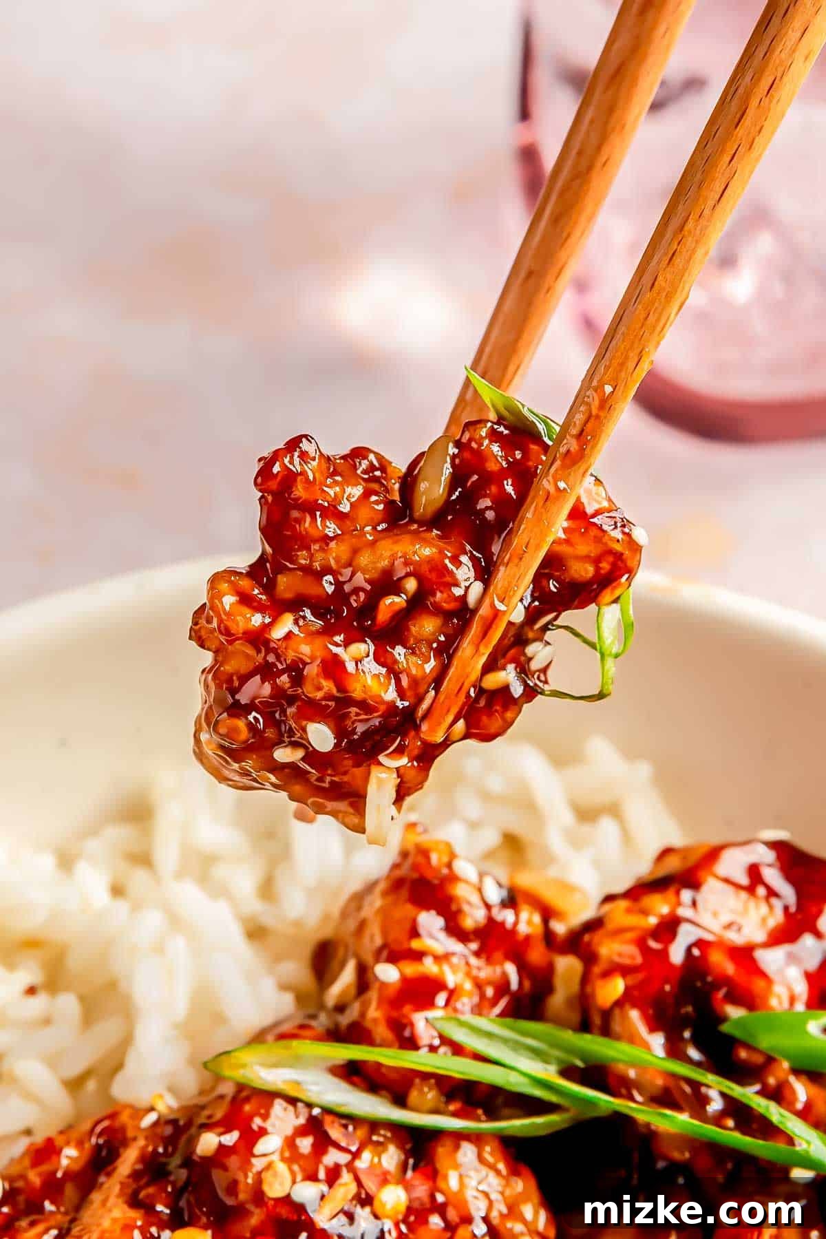 Zesty Crispy General Tsos 4 a pair of wooden chopsticks holding a piece of saucy general tso's chicken