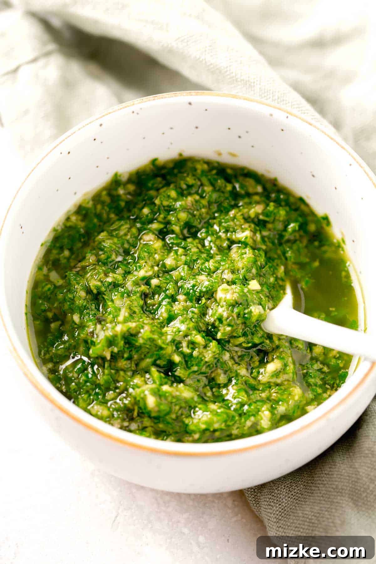 Vibrant green basil pesto in a small, elegant gold-rimmed bowl, with a white spoon resting inside, ready to be enjoyed.