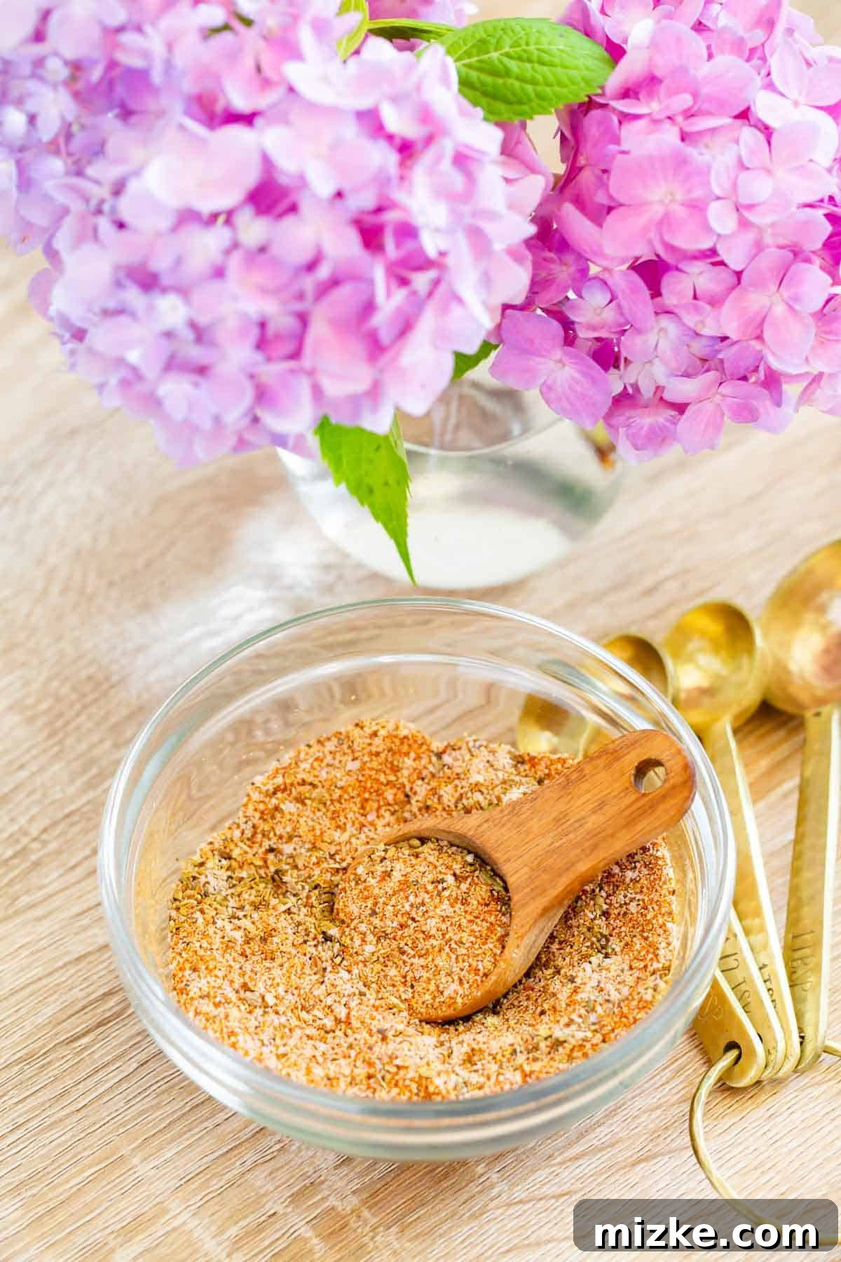 Signature Adobo Spice Blend 3 adobo seasoning in a wooden spoon next to pink hydrangeas