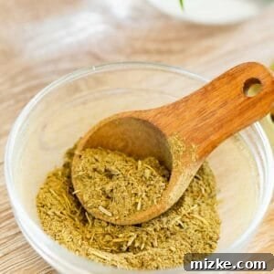 Homemade poultry seasoning in a wooden spoon, resting in a clear glass bowl, ready for cooking.