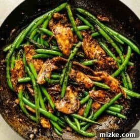Thickened stir-fry sauce coating chicken and green beans in the wok, creating a glossy finish.