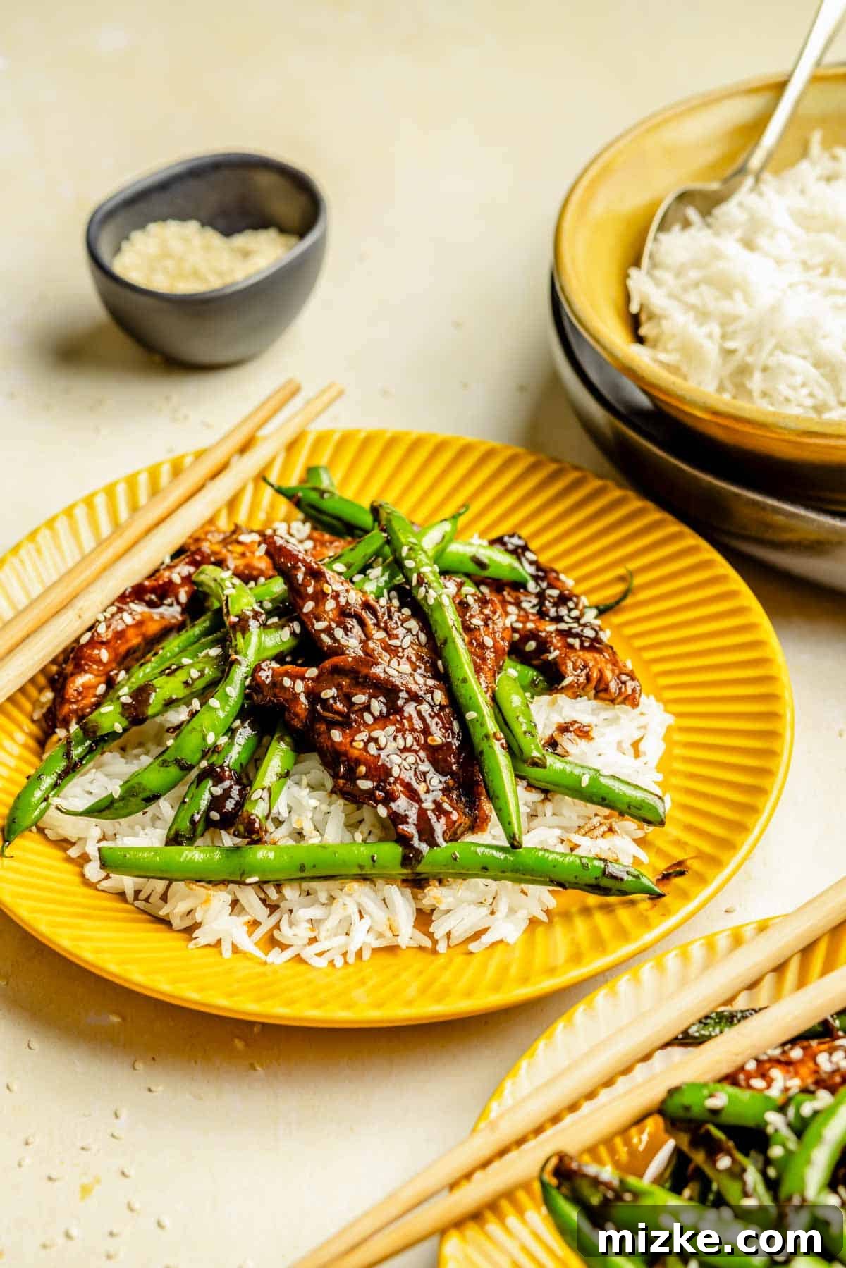 Chicken Stir Fry with Crisp Green Beans 4 A generous serving of Green Bean Chicken Stir Fry with white rice, accompanied by wooden chopsticks on a yellow plate.