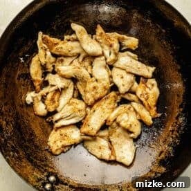 Thinly sliced chicken breast being cooked in a wok, achieving a golden brown exterior.
