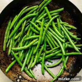 Green beans being charred and cooked in a wok, showing slight blistering on their surface.