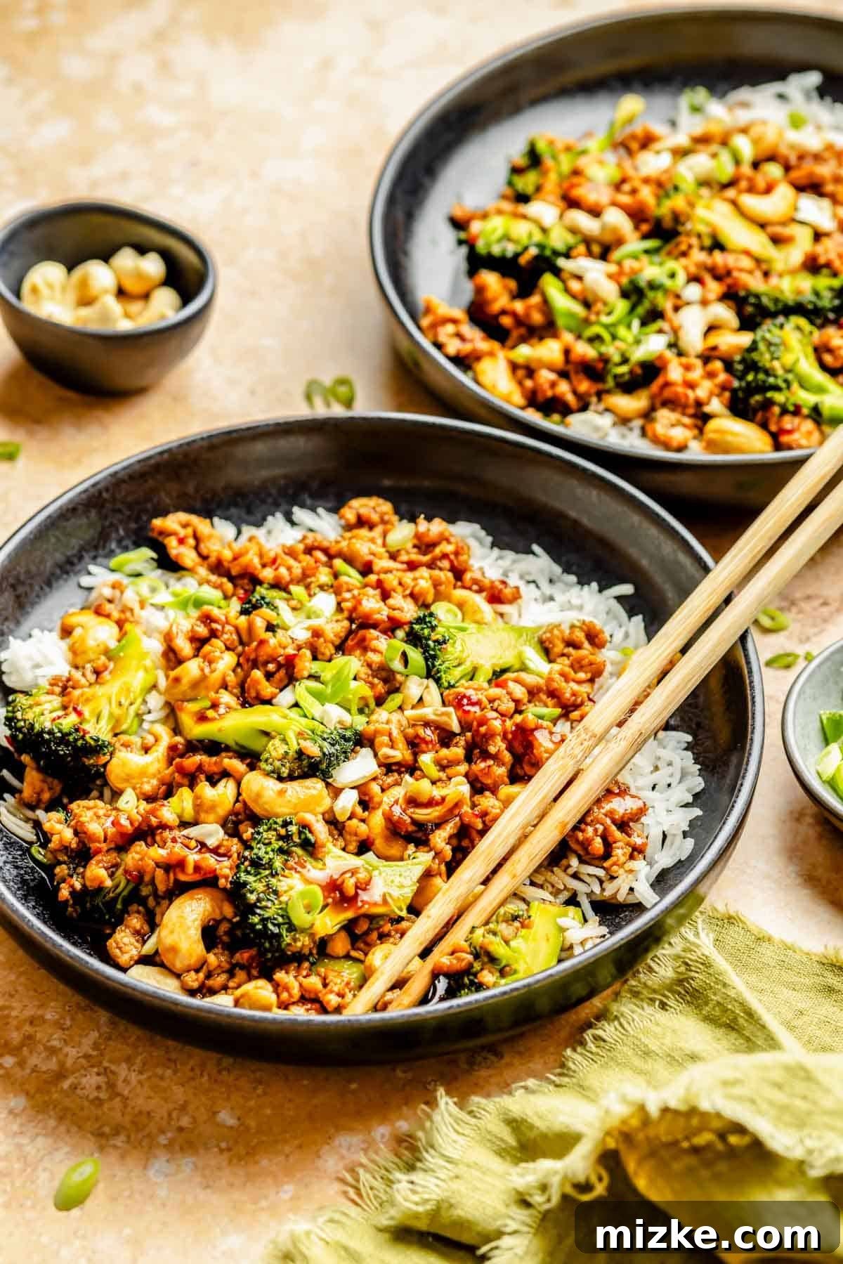 Crunchy Cashew Chicken with Vibrant Broccoli 3 A black bowl filled with white rice, topped generously with cashew chicken and broccoli stir fry, ready to be enjoyed with wooden chopsticks.