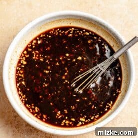 sauce ingredients for cashew chicken and broccoli stir fry in a white bowl with a metal whisk