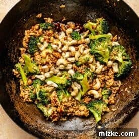 cashews added to the ground chicken and broccoli in the wok with sauce