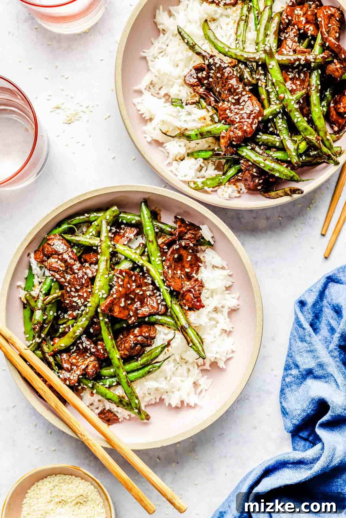 Sizzling Beef and Green Bean Stir-Fry 2 Two aesthetically arranged pink bowls, each filled with a generous portion of Green Bean Beef Stir Fry, served alongside fluffy white jasmine rice and traditional wooden chopsticks.