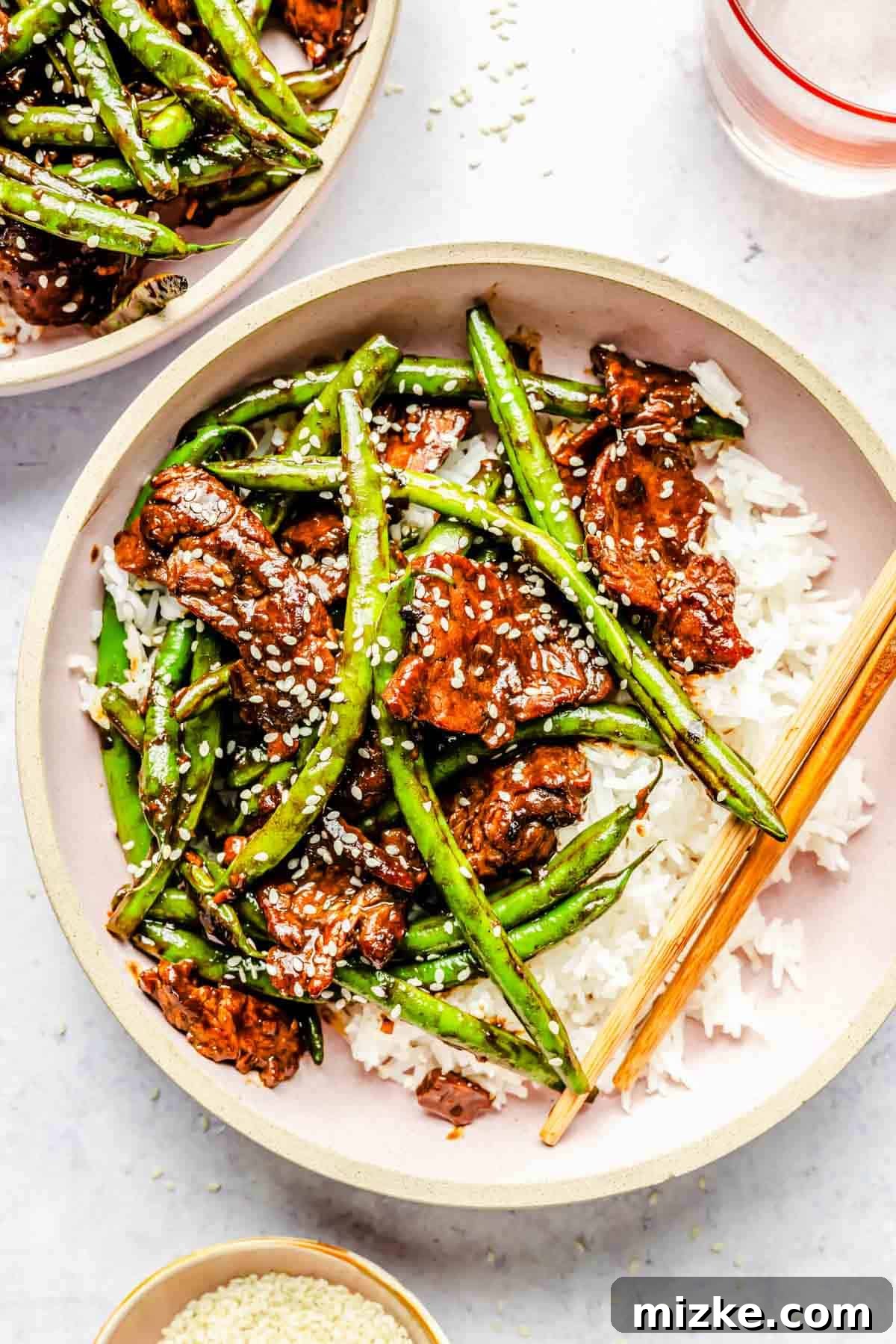 Sizzling Beef and Green Bean Stir-Fry 3 A close-up view of a single pink bowl showcasing the beautifully cooked Green Bean Beef Stir Fry, complete with white rice and wooden chopsticks, highlighting its delicious texture and vibrant colors.