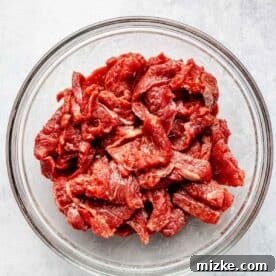 Sizzling Beef and Green Bean Stir-Fry 6 Thinly sliced flank steak marinating in a clear bowl with cornstarch, soy sauce, baking soda, and water, preparing for tenderness.