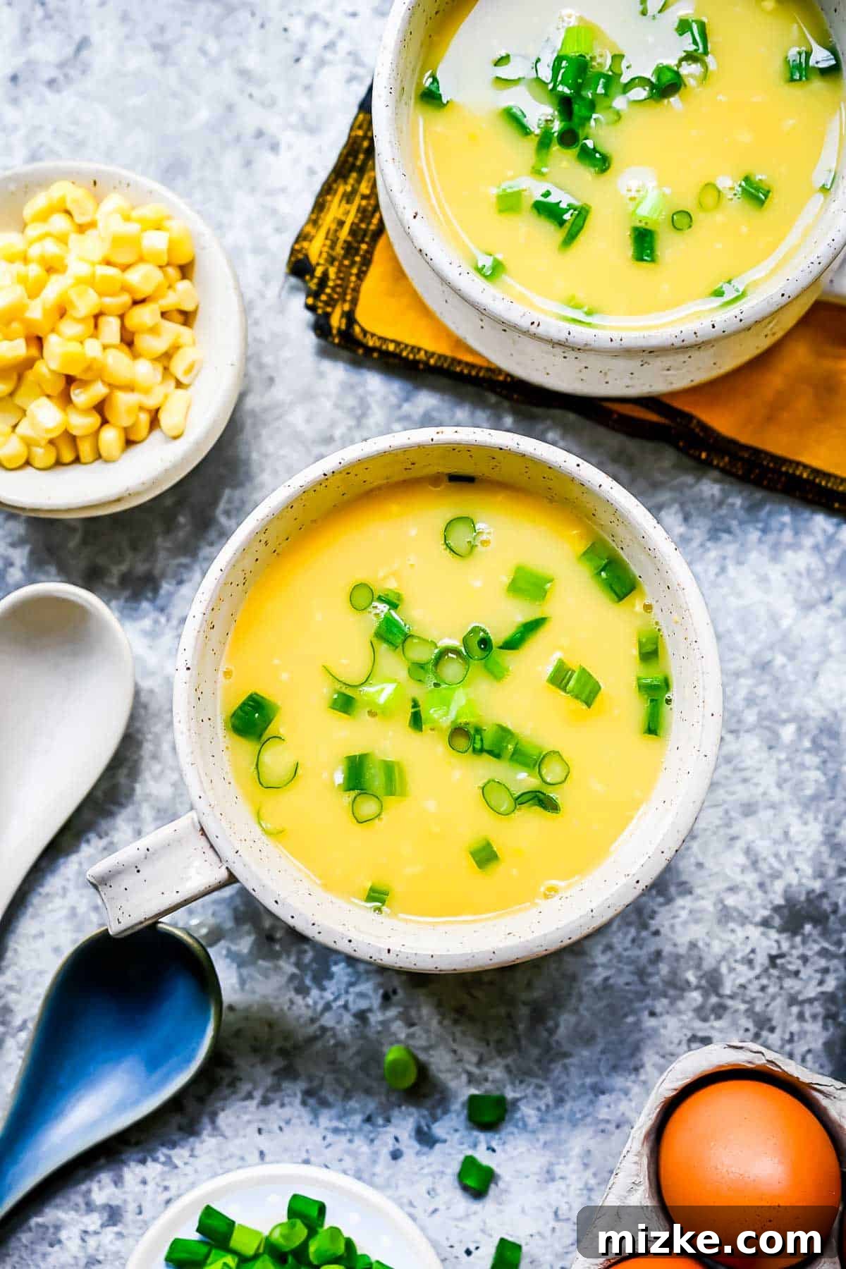 creamed corn and egg soup in mugs with fresh green onions on top, ready to be served