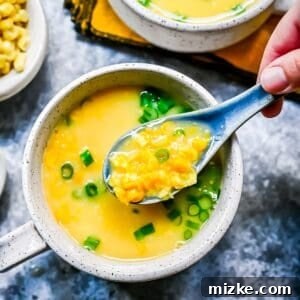 a soup spoon is filled with creamed corn and egg soup and many corn kernels, close up