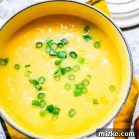corn soup mixture in a sauce pot with fresh scallions on top, eggs being stirred in