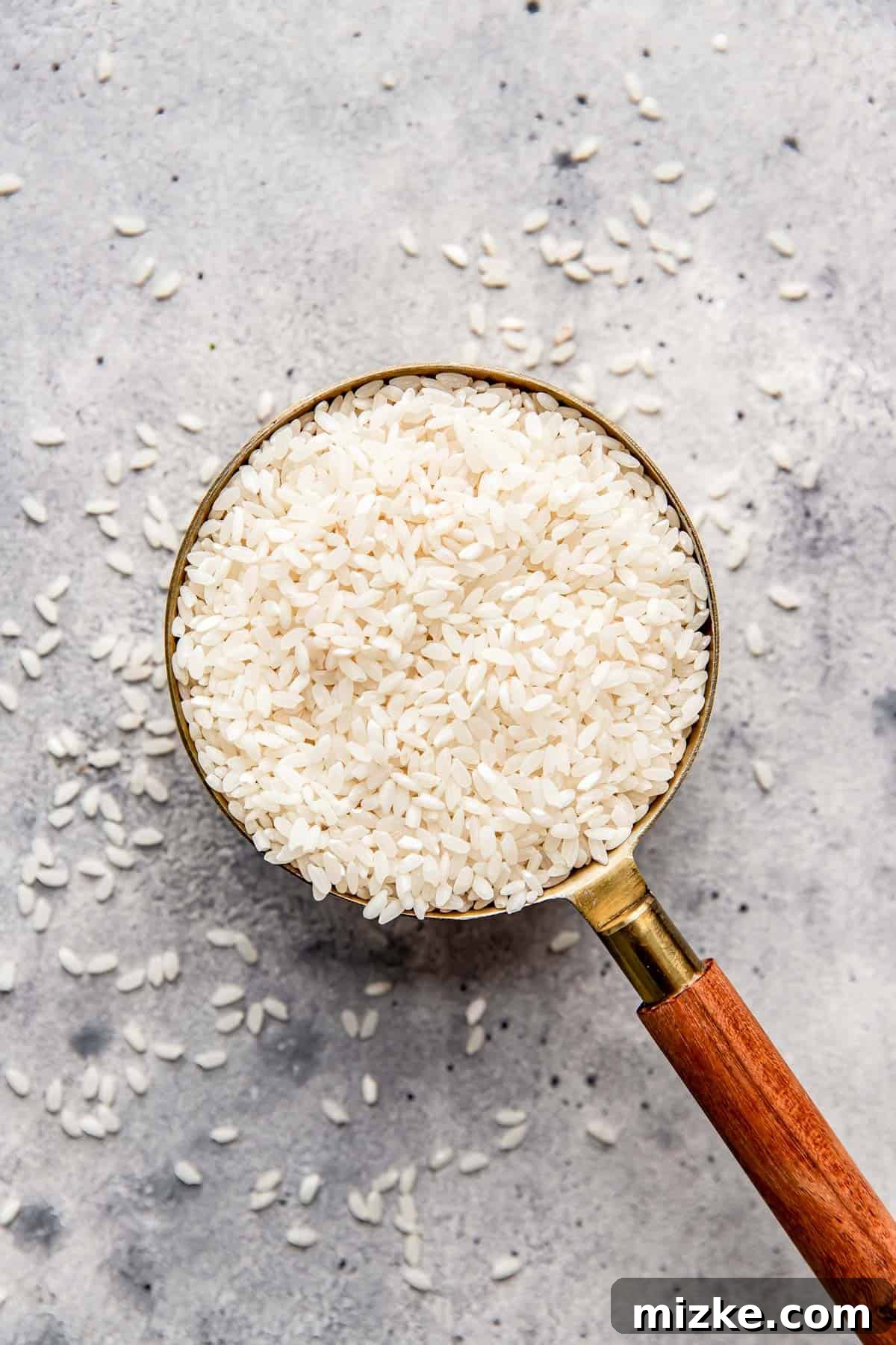 The Secret to Perfectly Fluffy White Rice 4 A charming wooden-handled measuring cup filled to the brim with medium grain white rice, with a few grains gracefully overflowing.