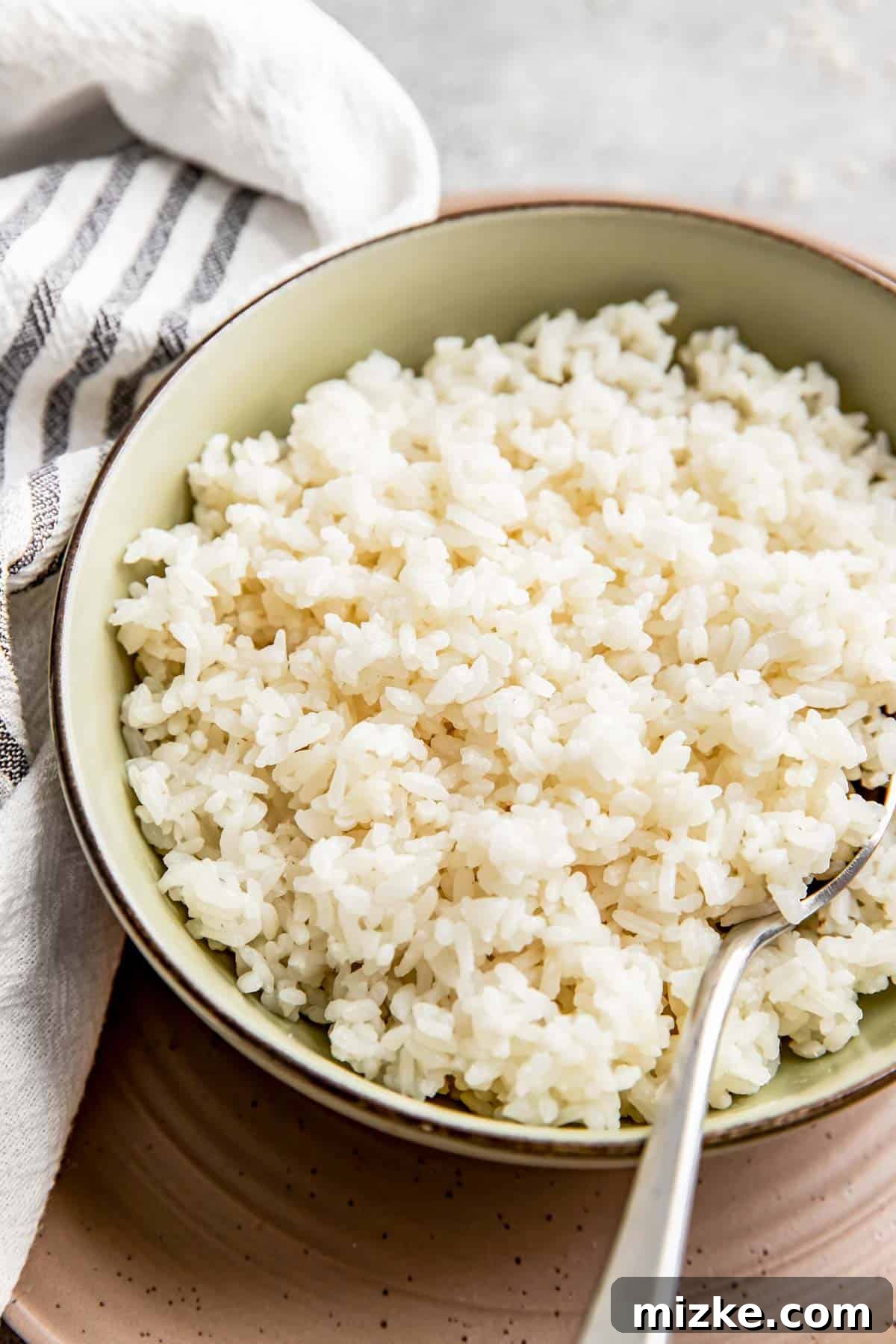 The Secret to Perfectly Fluffy White Rice 5 A vibrant green bowl filled with beautifully cooked white rice, placed next to a gleaming metal spoon, creating an appetizing scene.