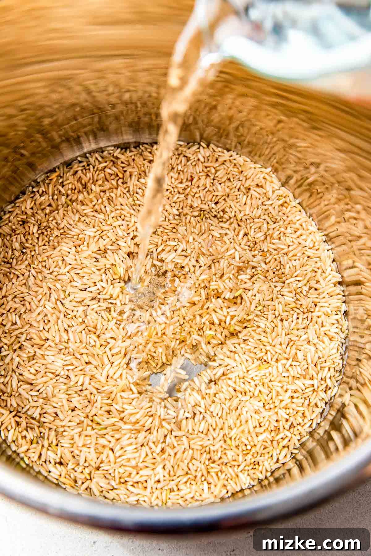 Perfect Brown Rice Every Time 3 uncooked brown rice is inside a stainless steel pot with water being poured inside