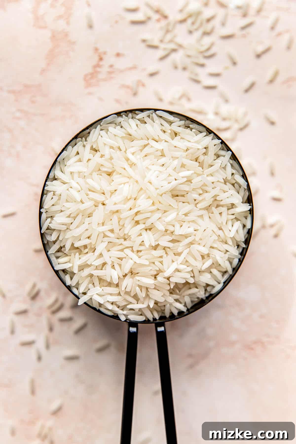 Secrets to Perfectly Fluffy Jasmine Rice 2 A black measuring cup holds a generous portion of uncooked jasmine rice, showcasing its delicate, long grains.